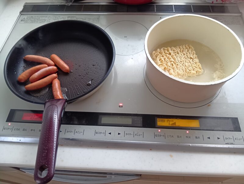 システムキッチンのコンロに、二つのティファール。左はフライパンでソーセージを焼き、右の鍋でラーメンを煮る。フライパンと鍋があった方が利便性高い比較写真