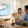 リビングでテレビショッピングのエアコン紹介を見ながらお得さについて相談する日本人の夫婦